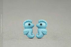 two blue seahorse shaped earrings sitting on top of a gray surface next to each other