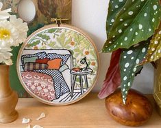 a close up of a embroidery on a table near a vase with flowers and a potted plant