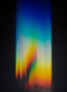 a blurry image of two people standing in front of a colorful light beam on a wall