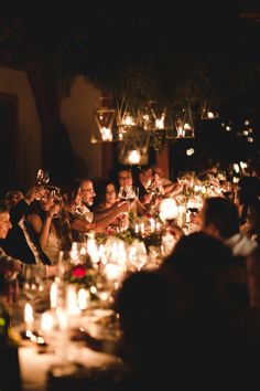 a group of people sitting around a dinner table with wine glasses and candles in front of them