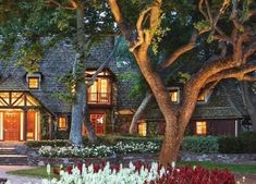 a large house with lots of trees and flowers in the front yard at night time