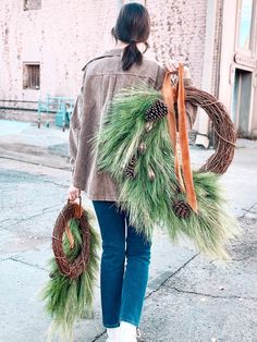 a woman is walking down the street with wreaths and pine cones on her back