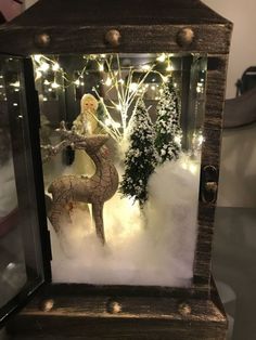 a glass case with a christmas scene in the snow and lights behind it is a deer