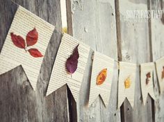 some leaves are hanging on the side of a wooden fence with paper garlands attached to it