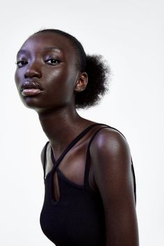 a woman with dark skin wearing a black tank top and standing in front of a white background