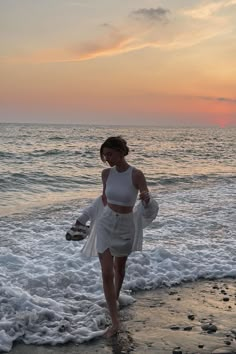 a woman walking on the beach at sunset