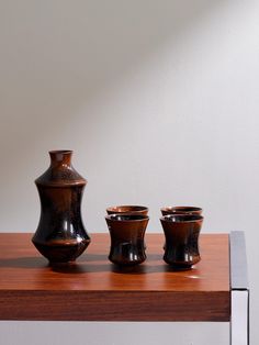 three brown vases sitting on top of a wooden table next to a white wall