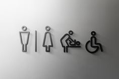 three metal signs depicting different types of toilet and urinals on a white wall