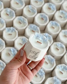 a hand holding a small white cup with blue flowers on it and a ring in the middle