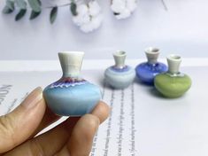 a hand holding a miniature vase in front of three smaller ones