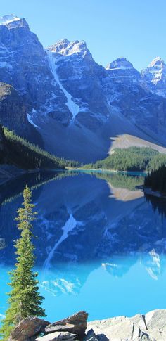 a mountain lake surrounded by snow covered mountains and pine trees in the foreground, with blue water below