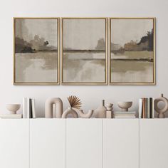 three paintings hanging on the wall above a white cabinet with books and vases in front of it