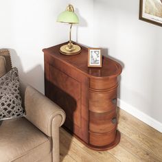 a wooden cabinet sitting next to a chair in a room with white walls and wood flooring