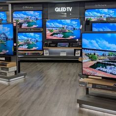 several televisions on display in a store with wooden floors and gray walls, all displaying different types of tv's