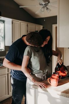 a man and woman standing in a kitchen next to an orange mug on a counter