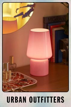 a pink lamp sitting on top of a wooden table next to a bottle of perfume