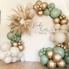 a baby shower is decorated with gold and green balloons, greenery, and a wreath