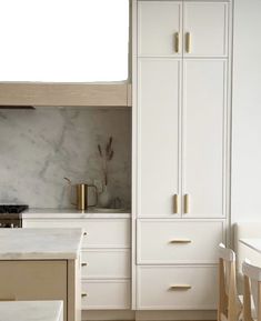 a kitchen with white cabinets and marble counter tops