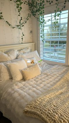 a bed with white sheets and pillows in a bedroom next to a plant hanging on the wall