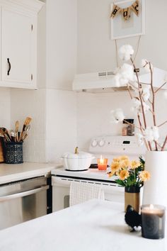 a white kitchen with flowers and candles on the counter top in front of an oven