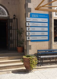 a bench sitting in front of a building next to a tall planter filled with flowers