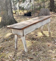 an old wooden bench sitting in the middle of a field next to a tree and a black dog