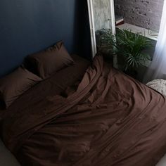 an unmade bed with brown sheets and pillows in front of a brick wall next to a window