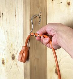 a person is holding an orange cord and pulling it out of a wooden door with a pair of scissors