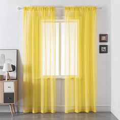 a yellow curtain hanging in front of a window with white walls and wooden flooring