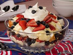 a bowl filled with fruit and whipped cream on top of a patriotic table cloth next to silverware