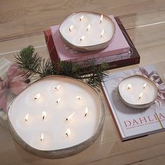 two white candles sitting on top of a table next to a book and christmas tree