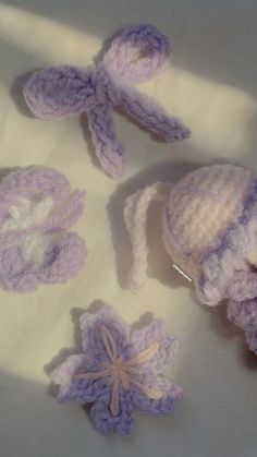 three crocheted hats and two flowers on a white cloth surface with shadows from the sun