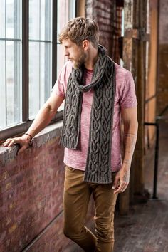 a man standing next to a brick wall wearing a scarf and looking out the window