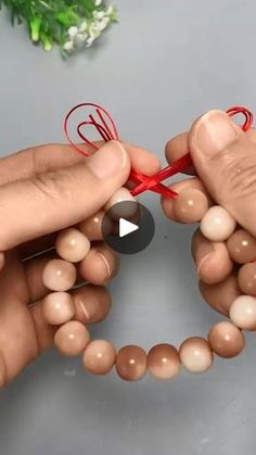 two hands holding red string and making a heart shaped decoration with small balls on it