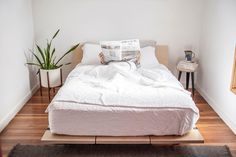 a white bed sitting in a bedroom next to a wooden table with a potted plant on top of it