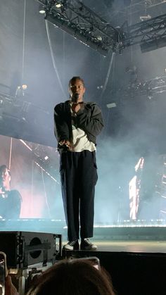 a man standing on top of a stage with his hands in his pockets as he sings