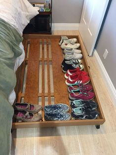 there are many pairs of shoes in the drawer on this bed frame that is made out of wooden slats