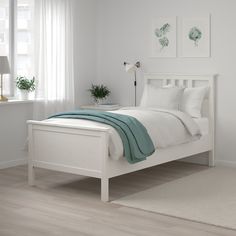 a white bed sitting in a bedroom on top of a hard wood floor next to a window