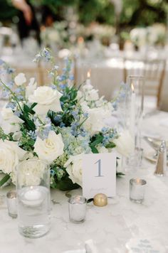 the table is set with white and blue flowers in vases, candles, and place cards