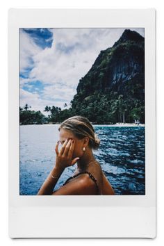 a polaroid photo of a woman sitting on a boat in the water with mountains in the background