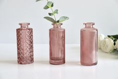 three pink vases with flowers in them on a white table next to each other