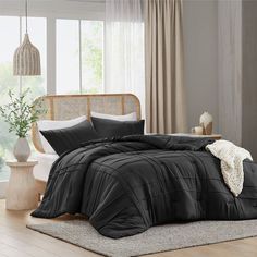 a bed with black comforter and pillows in a room next to a window,