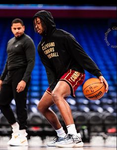 two basketball players in black hoodies and red shorts are on the court, one is holding a basketball