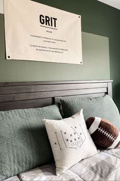 a football pillow sitting on top of a bed next to a framed sign that reads grit