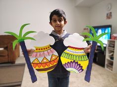 a young boy holding up two paper cut outs with palm trees in the middle and clouds above them