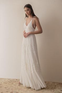 a woman wearing a white dress standing in front of a beige wall with her hand on her hip