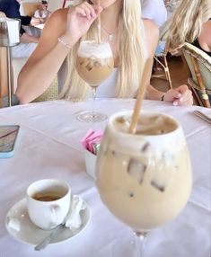 a woman sitting at a table with a drink in front of her and two cups on the table