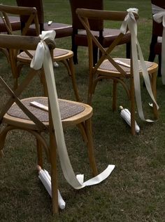 several chairs with white ribbons tied to them on the grass in front of some trees