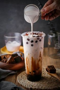 someone pouring milk into a cup with chocolate and marshmallows in it on a wooden table