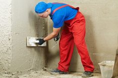 a man in blue shirt and red pants working on a cement wall with a drill